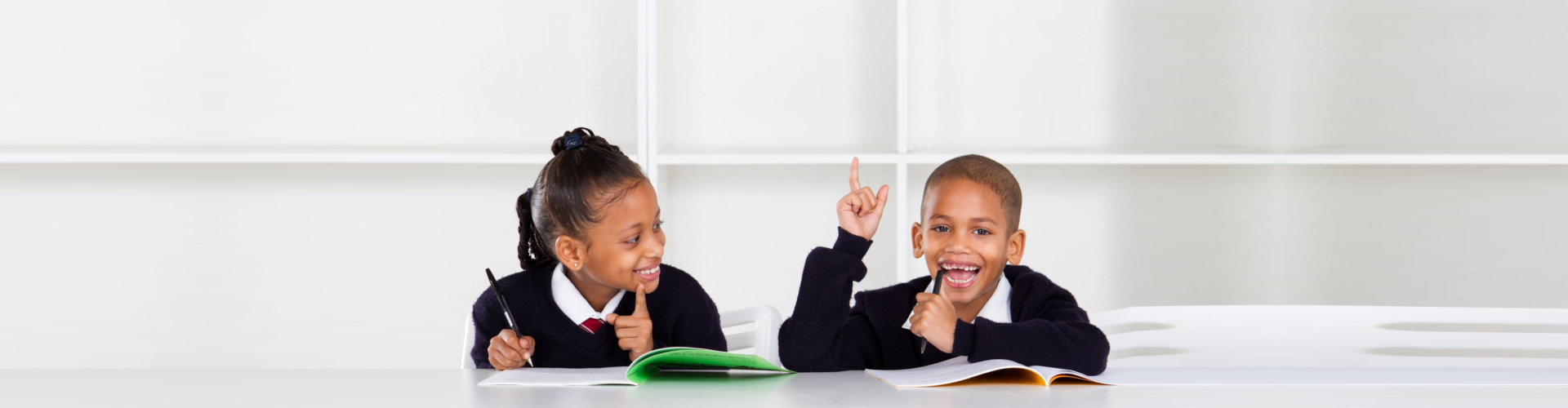 two children wearing uniforms while writing on their notebook